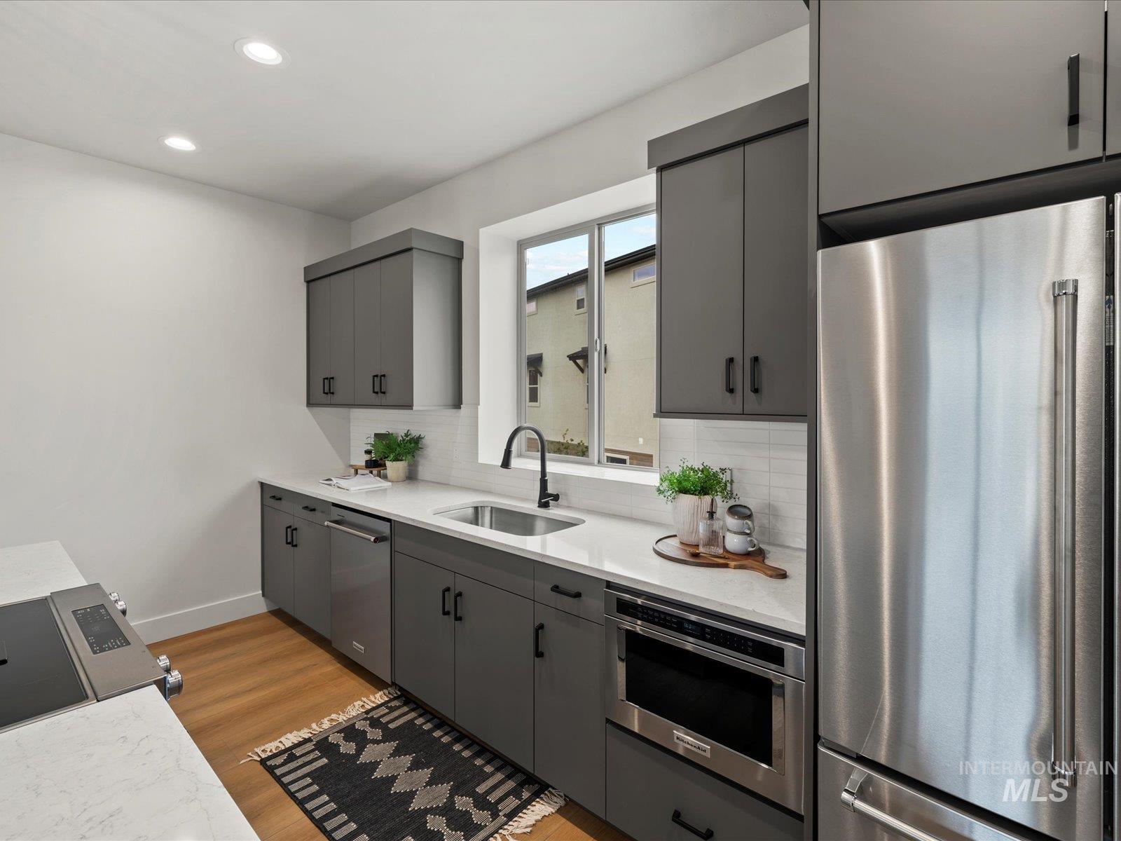 Kitchen with gray cabinetry, appliances with stainless steel finishes, light wood-style floors, backsplash, and recessed lighting