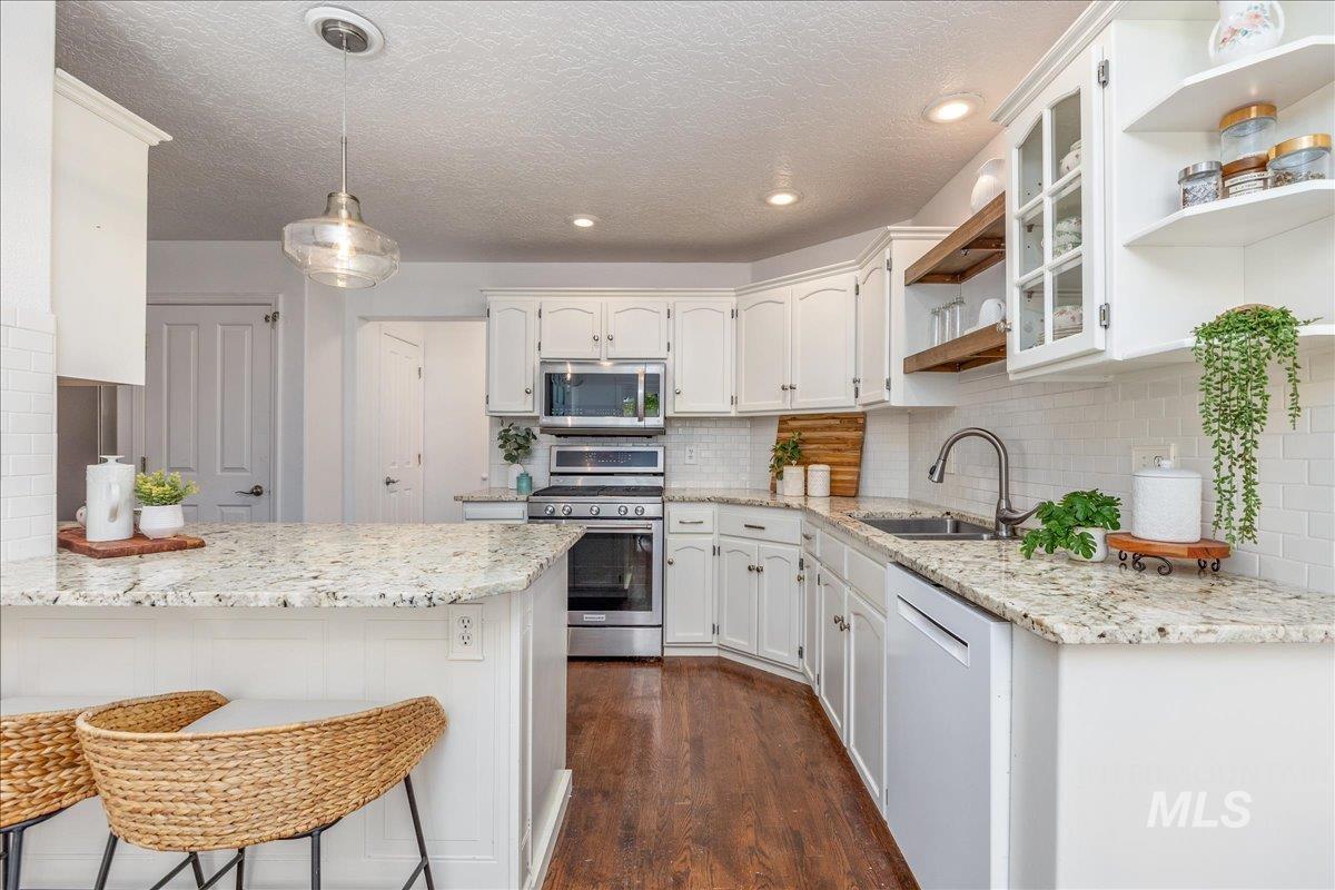 Kitchen featuring light-toned countertops, white cabinetry, a built-in stainless steel microwave and range, and dark wood-finish flooring