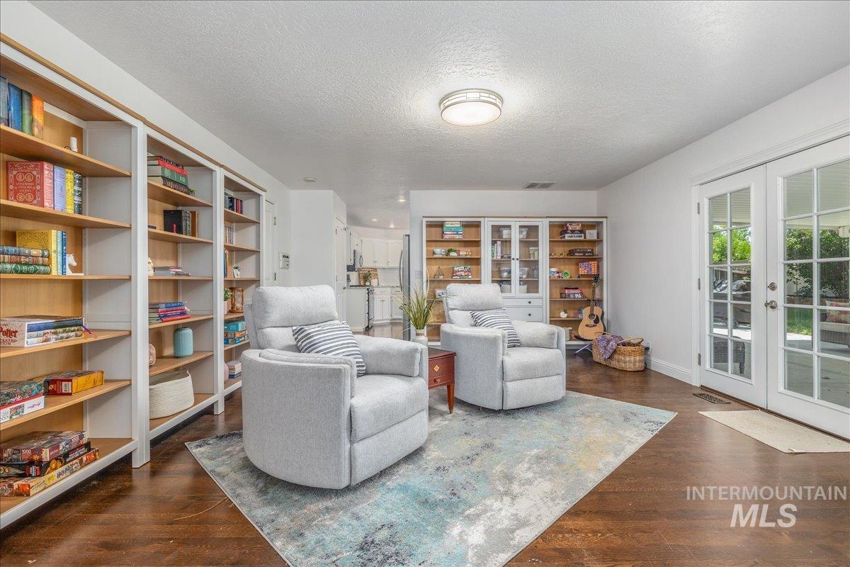Spacious living area featuring extensive built-in shelving, rich wood-finish flooring, and a pair of French doors providing exterior access