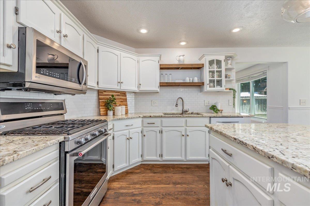 Kitchen featuring white cabinetry, light-toned countertops, stainless steel appliances, and wood-finish flooring