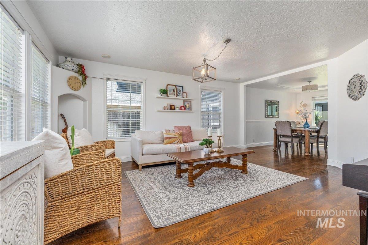 Spacious living area featuring rich wood-finish flooring, multiple windows providing natural light, a built-in arched alcove, and an open layout to a dining space