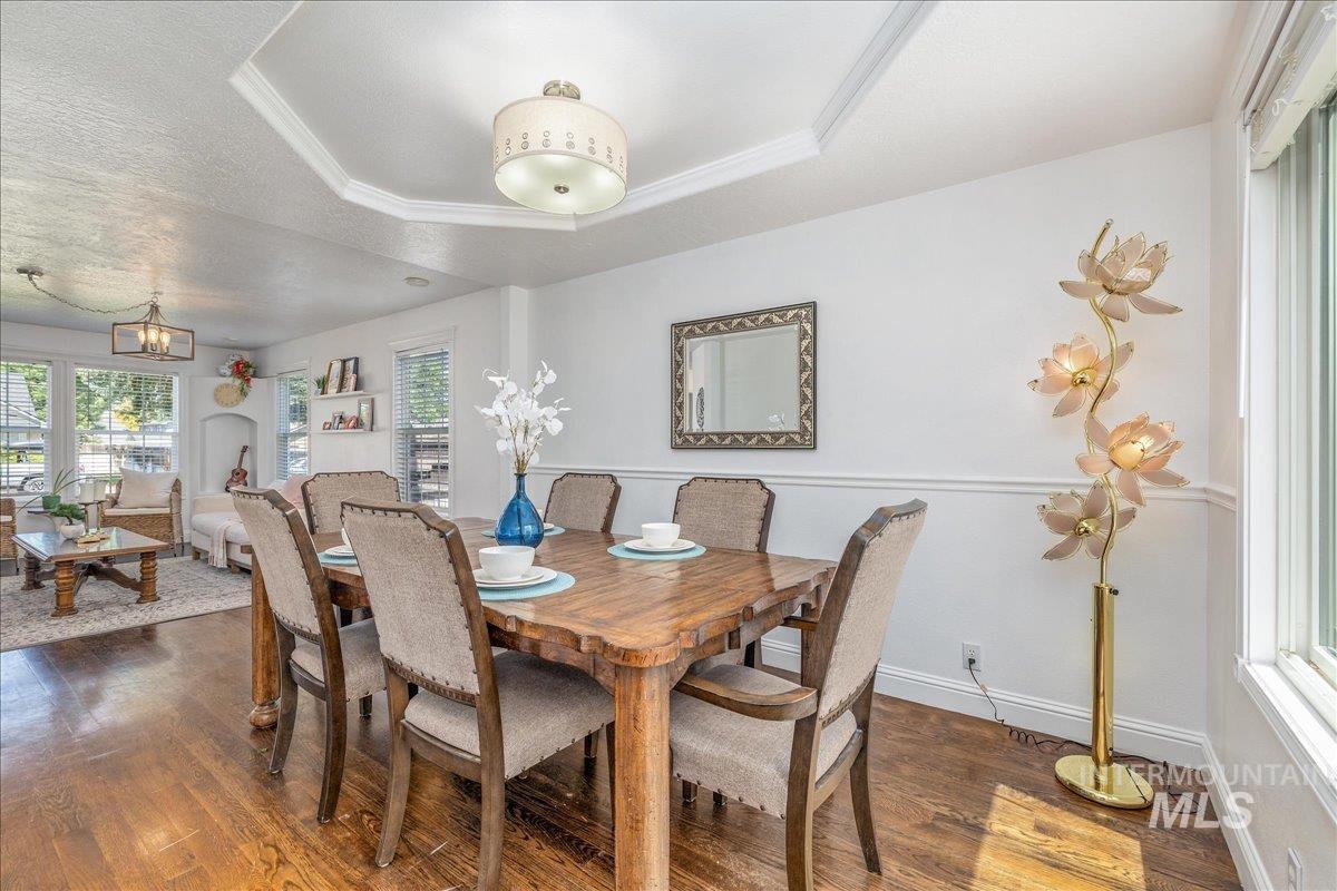 Dining area featuring wood-finish flooring, a tray ceiling with crown molding, and wainscoting