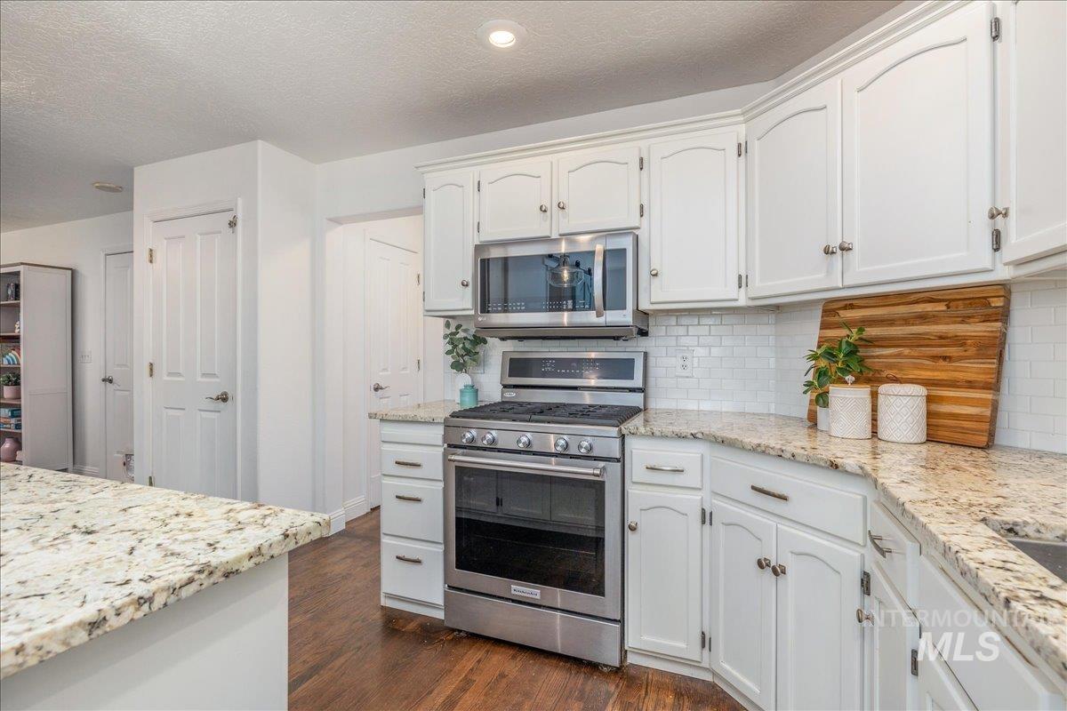 Kitchen featuring white cabinetry with silver hardware, granite countertops, and stainless steel appliances including an oven range and built-in microwave