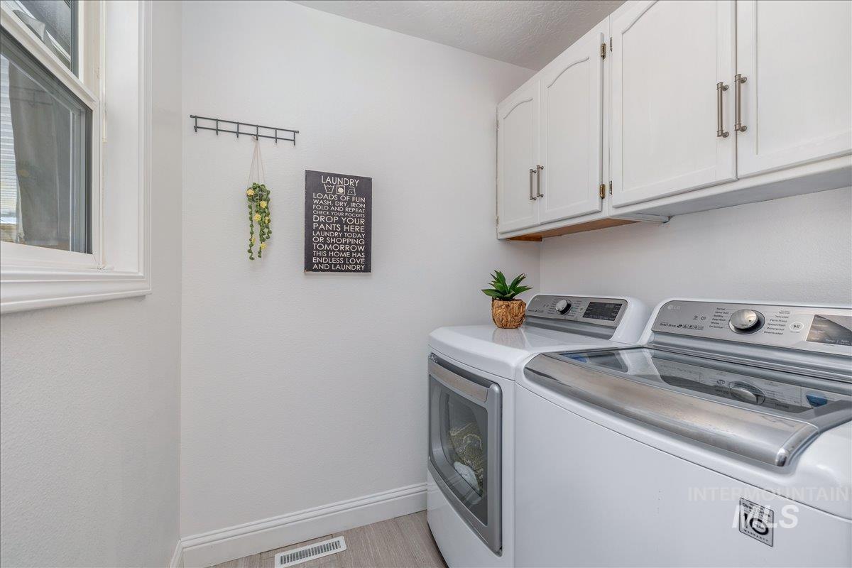 Dedicated laundry space featuring upper cabinetry with brushed nickel pulls, a window for natural light, and light wood-finish flooring
