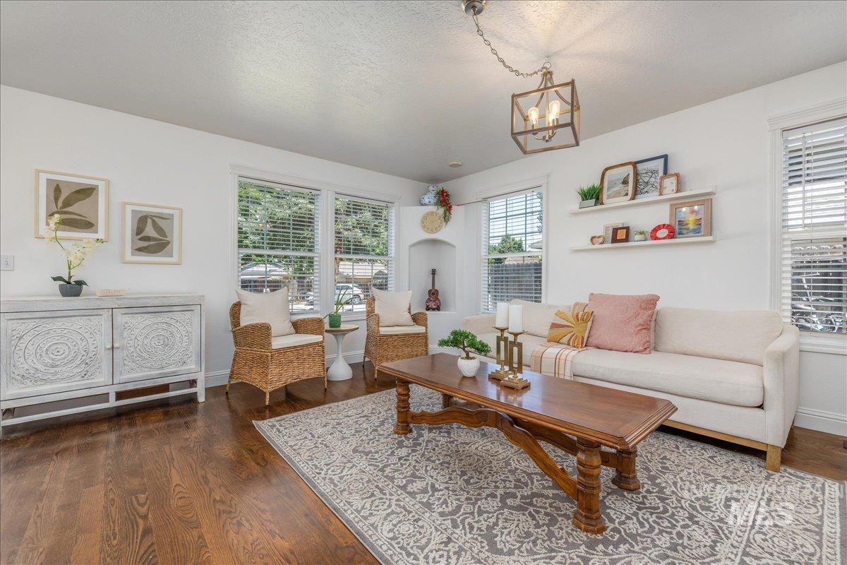 Inviting living area featuring rich wood-finish flooring, multiple windows with blinds, a built-in wall niche, two floating wall shelves, and an overhead decorative light fixture