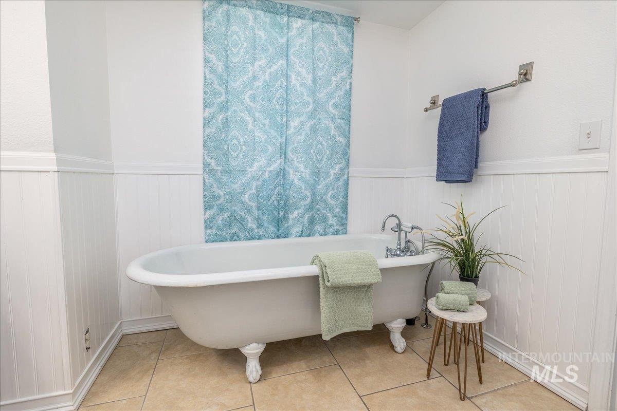Freestanding clawfoot bathtub with chrome fixtures, set against white beadboard paneling and neutral-toned tile flooring
