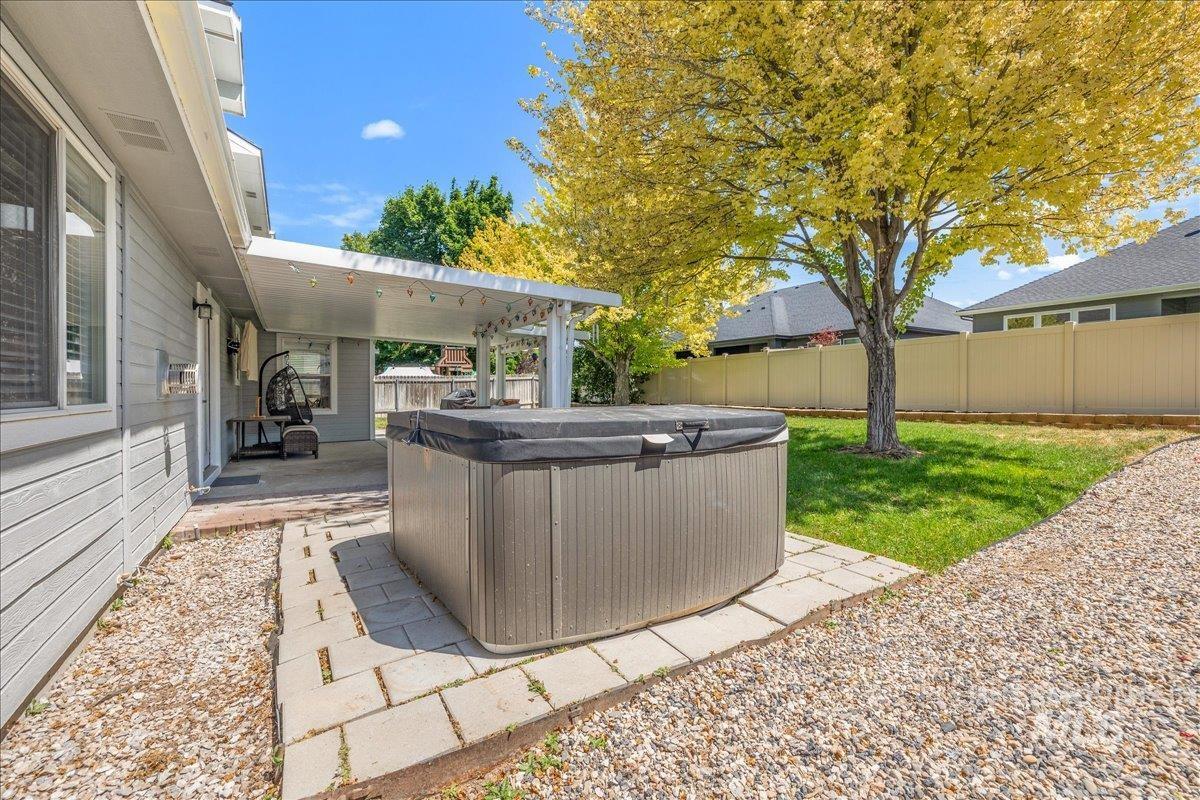 Private backyard featuring a hot tub on a paver patio, a covered patio area with string lights, and a fenced perimeter