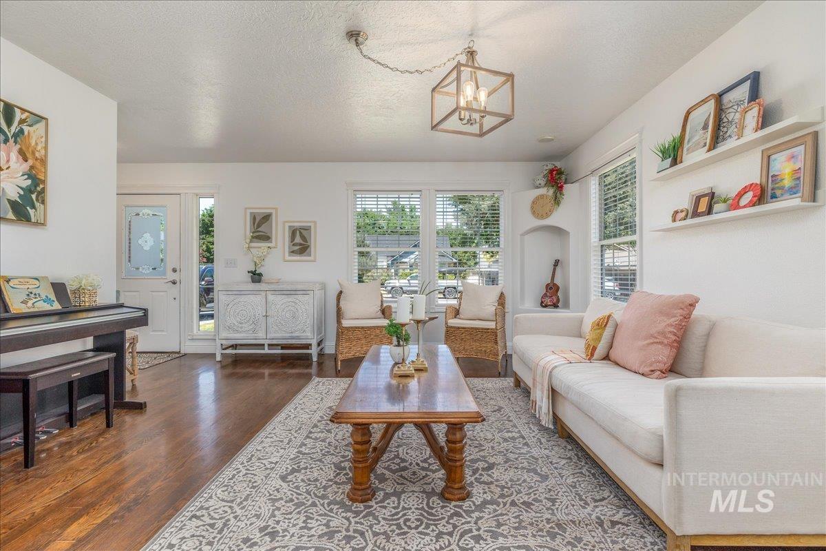 Spacious living area featuring wood-finish flooring, white walls, multiple windows with blinds, a recessed niche, and a contemporary ceiling light fixture