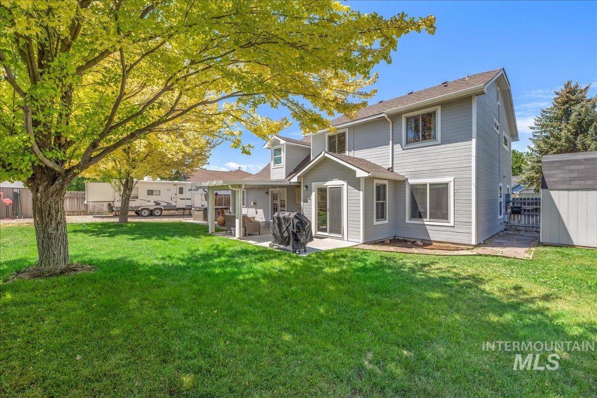 Expansive backyard featuring a manicured lawn, mature shade trees, a covered patio, and a utility shed