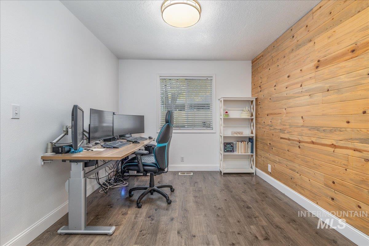 Dedicated room featuring a natural wood accent wall, neutral painted walls, wood-finish flooring, a window with blinds, and white baseboards