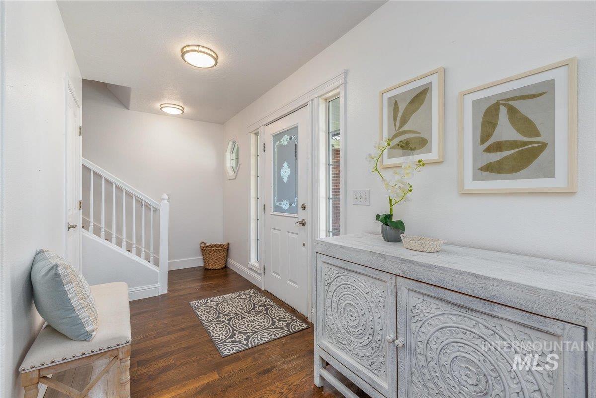 Entryway featuring wood-finish flooring, a white front door with decorative glass, and a staircase with white balusters