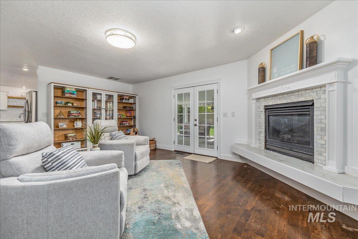 Living area featuring dark wood-finish flooring, a white mantel fireplace with tile surround, and built-in shelving with glass-front cabinetry
