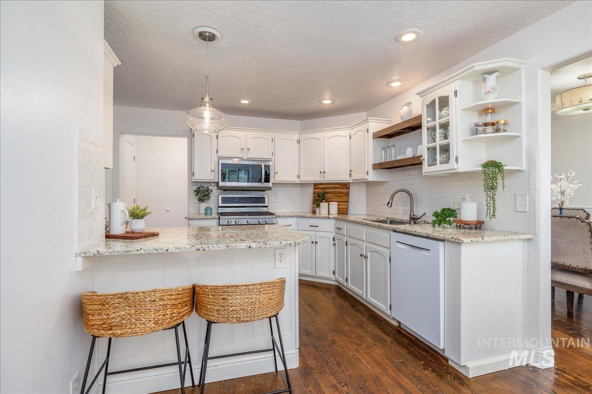 White kitchen featuring wood-finish flooring, white cabinetry, granite countertops, a white tile backsplash, and stainless steel appliances