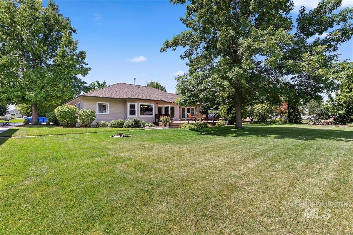 Spacious backyard with a substantial lawn, mature trees providing shade, and a wood deck extending from the residence