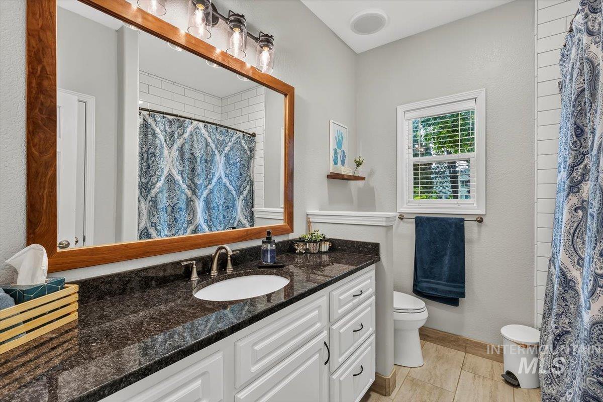 Bathroom featuring a dark stone countertop, undermount sink, white cabinetry with dark hardware, and a large wood-framed mirror