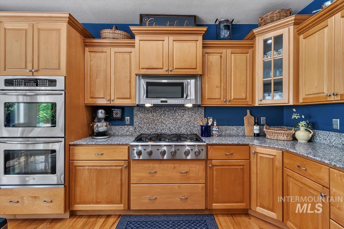 Kitchen featuring light wood cabinetry, stainless steel double wall ovens, a gas range, a built-in microwave, and speckled countertops