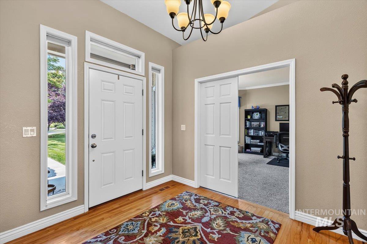 Entryway featuring wood-finish flooring, a paneled front door with sidelights and transom window, and a built-in chandelier