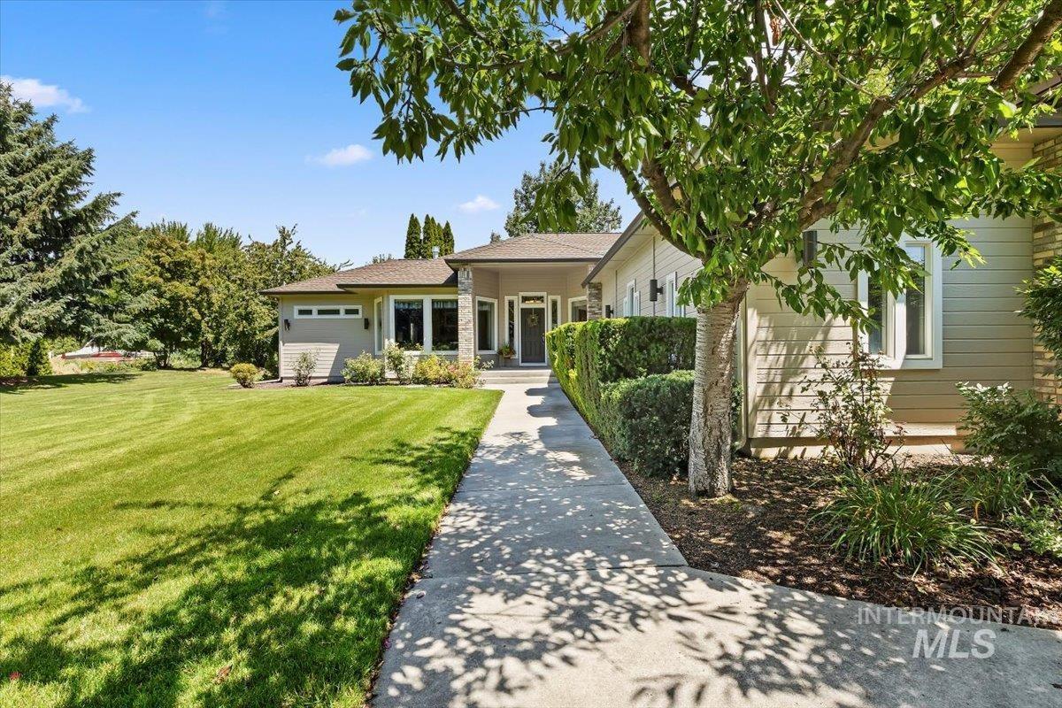 Contemporary-style residence featuring a prominent front entrance with a dark door, expansive front lawn, mature trees, and a concrete pathway