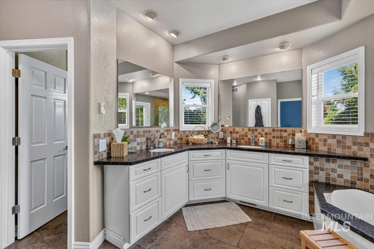 Bathroom featuring a double vanity with white cabinetry, dark stone countertops, and a full-width mirror