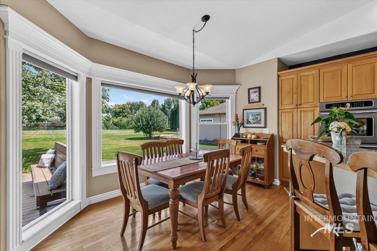 Hardwood flooring throughout a dining area featuring a bay window, built-in bench seating, and a chandelier