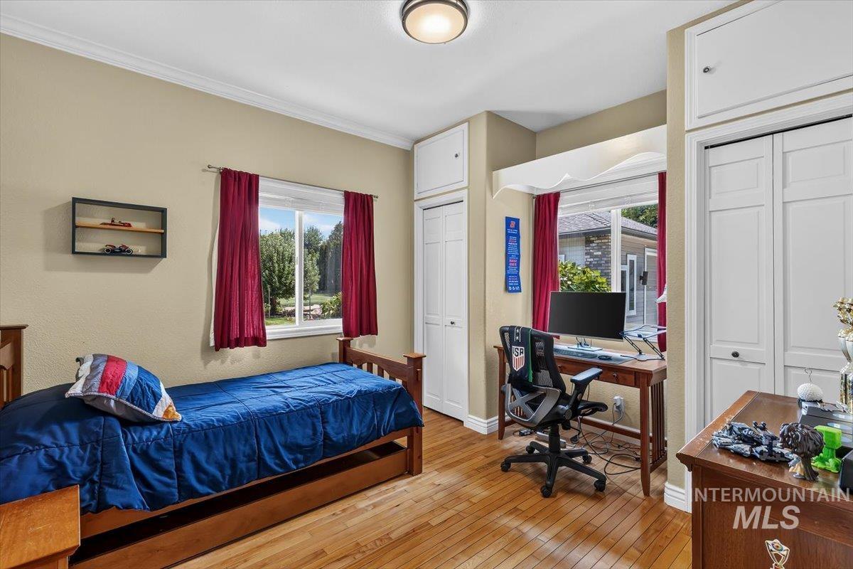 Hardwood flooring throughout this room, featuring a window with exterior landscaping, crown molding, and built-in closet storage with upper cabinetry