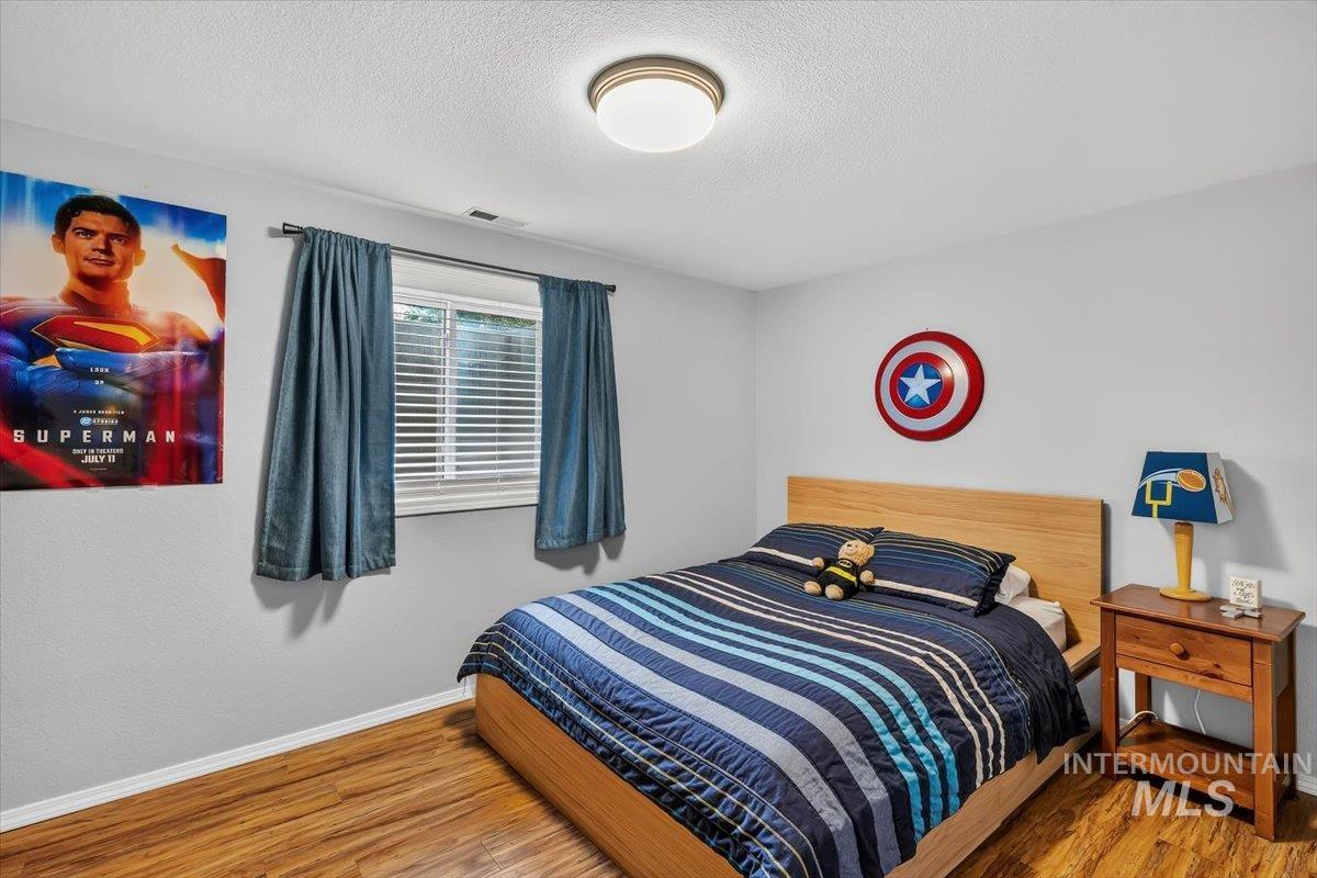 Room featuring wood-finish flooring, a window with horizontal blinds and drapery rods, and a ceiling-mounted light fixture