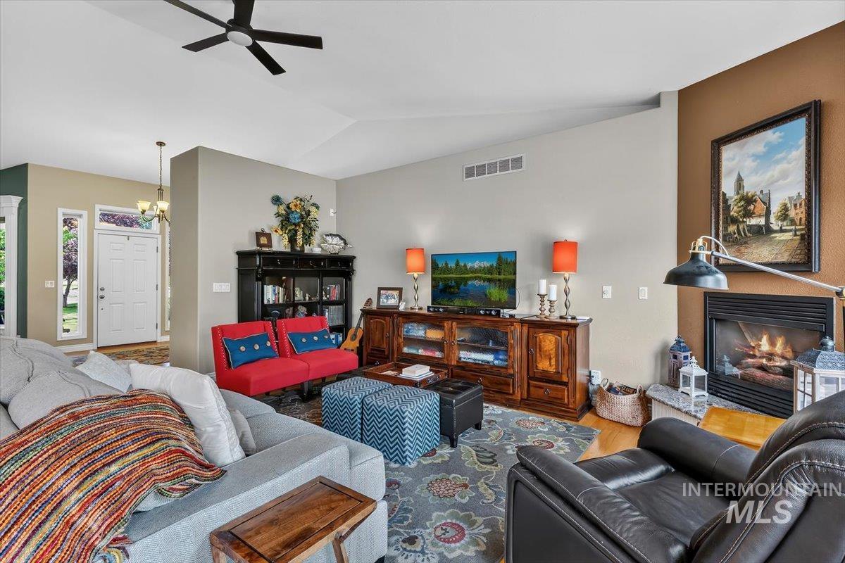 Living room featuring a fireplace, wood-finish flooring, vaulted ceilings, and a ceiling fan
