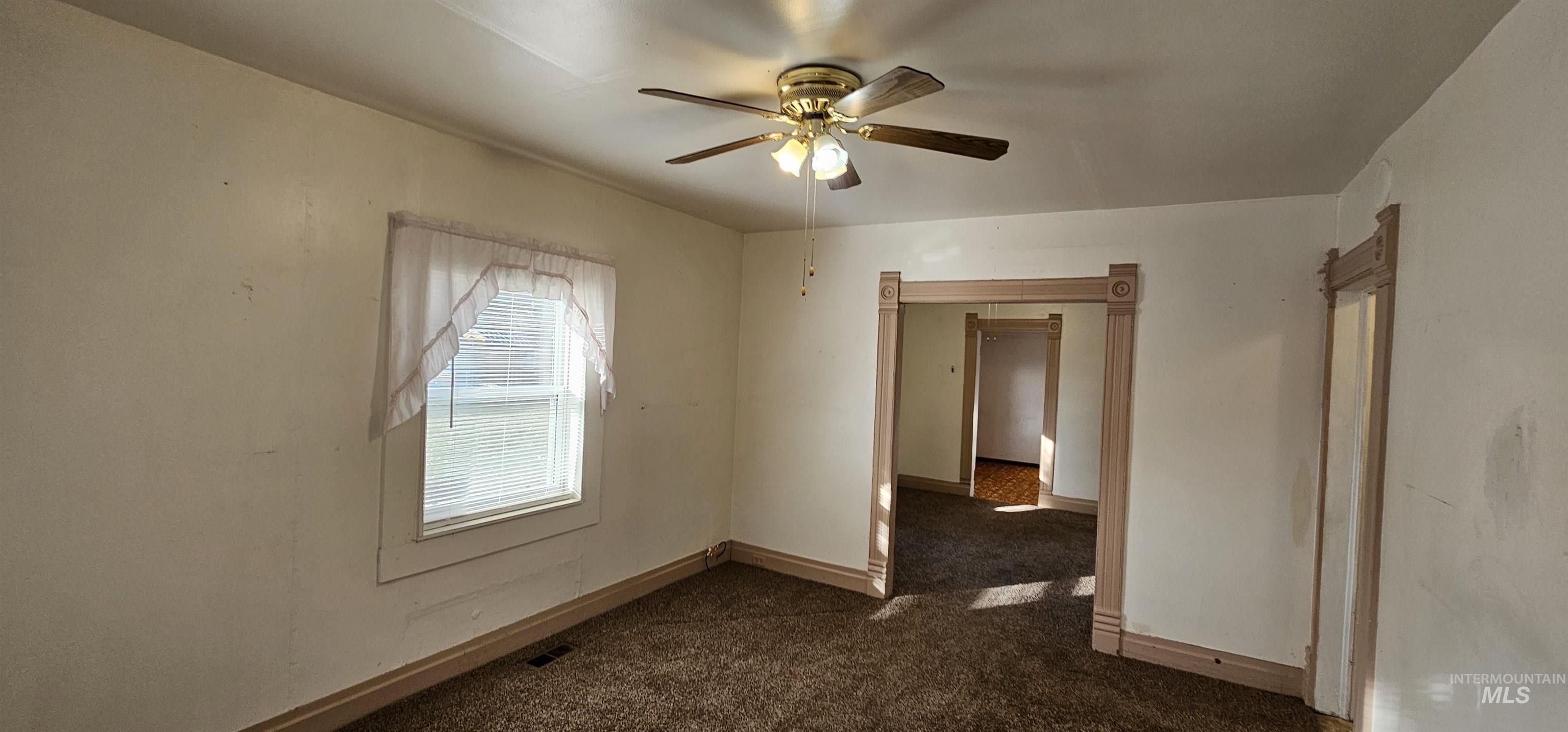 Unfurnished room with dark colored carpet and a ceiling fan