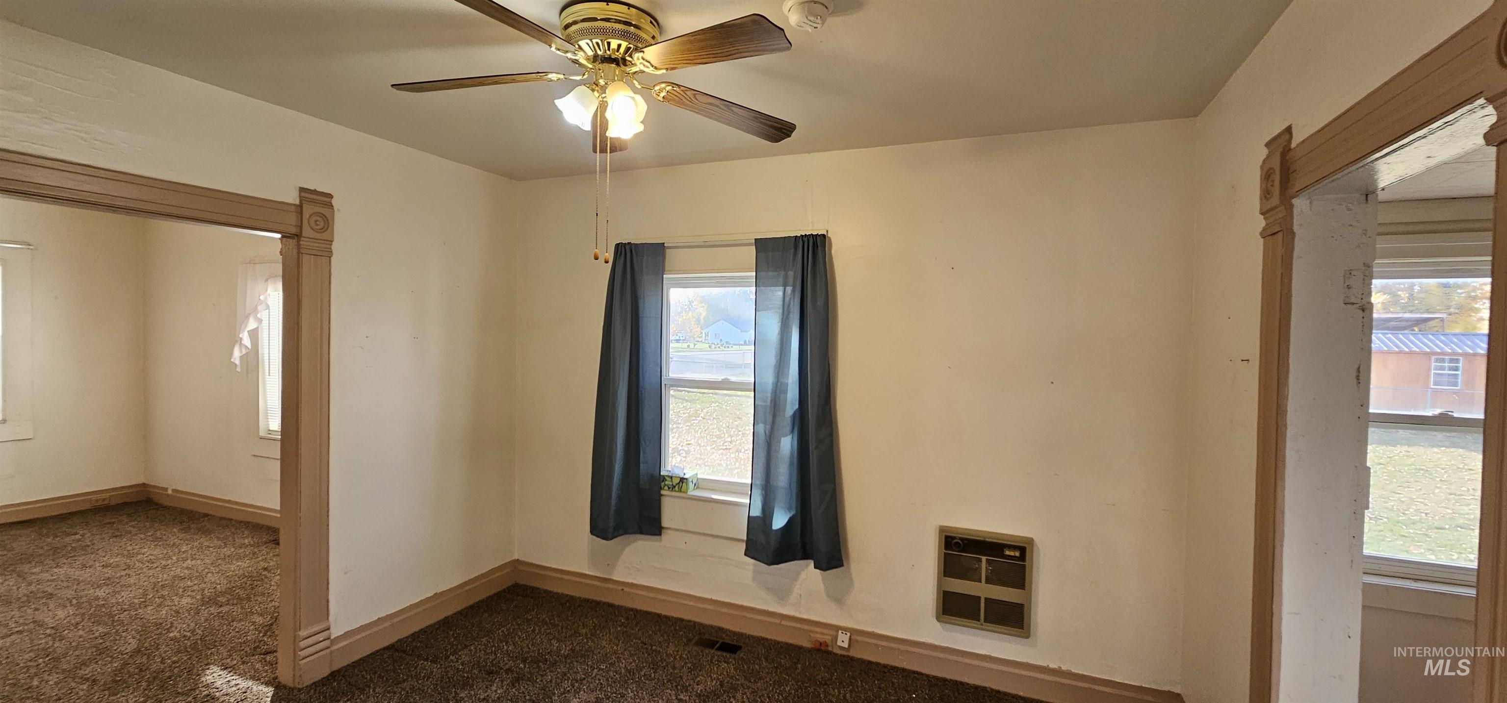 Empty room featuring dark carpet, heating unit, and ceiling fan