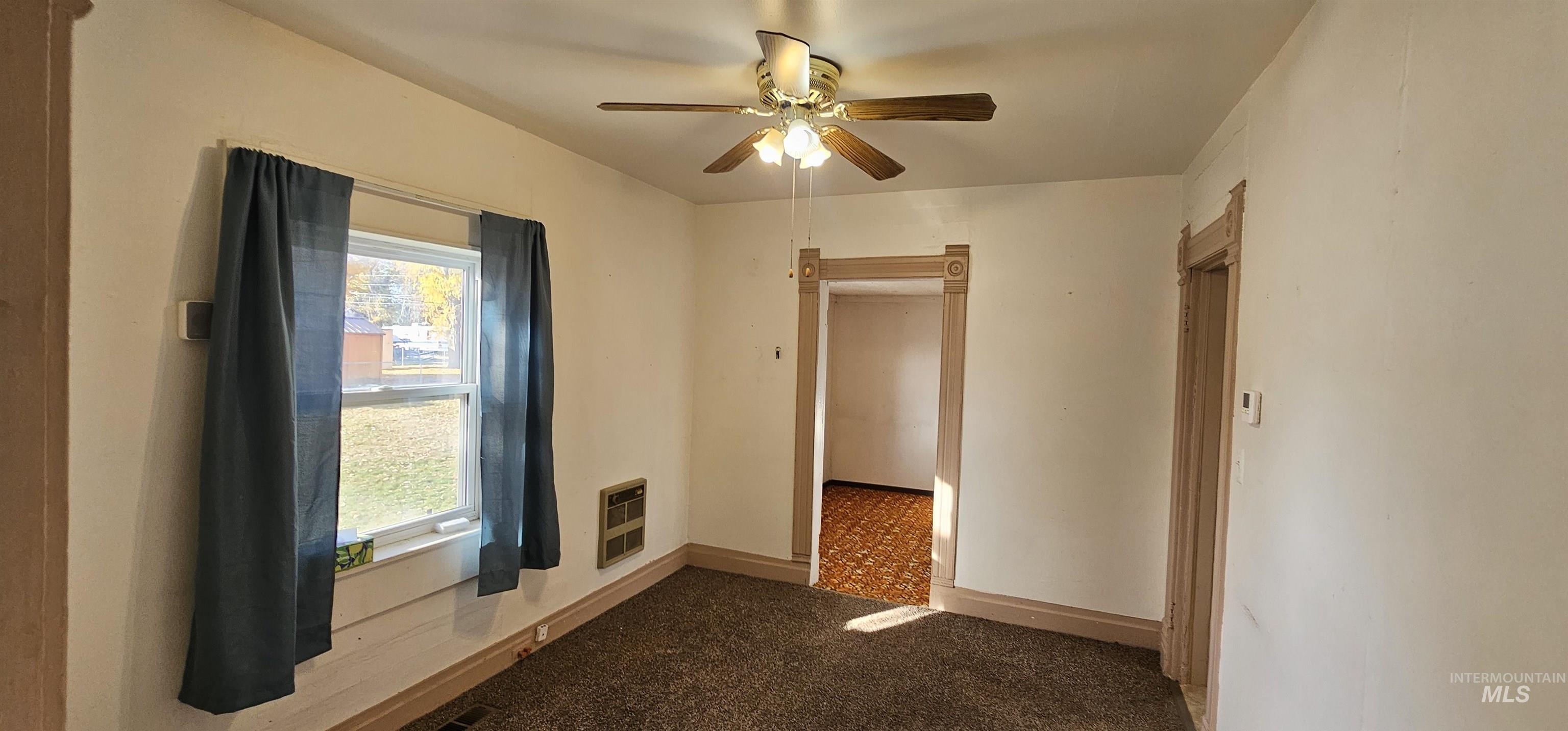 Spare room featuring dark colored carpet, ceiling fan, and heating unit