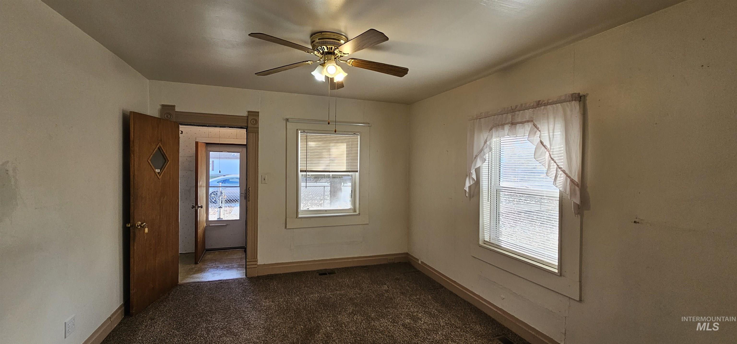 Unfurnished room featuring plenty of natural light, dark colored carpet, and a ceiling fan
