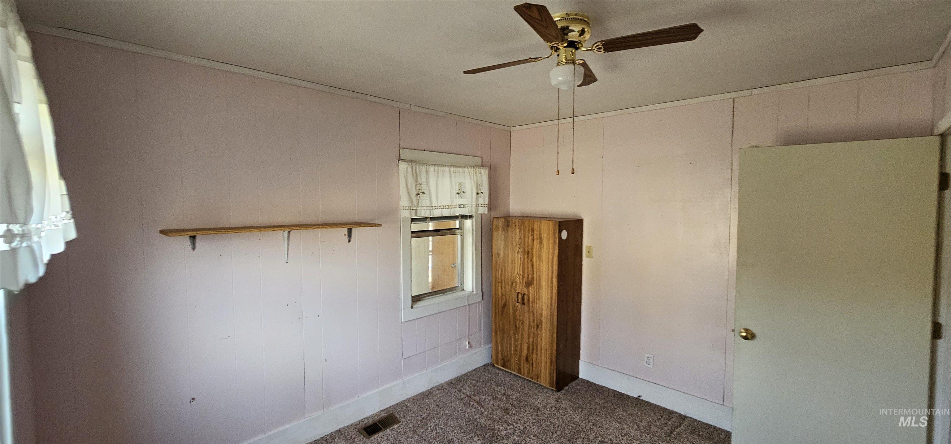 Empty room with crown molding, wood walls, ceiling fan, and dark colored carpet