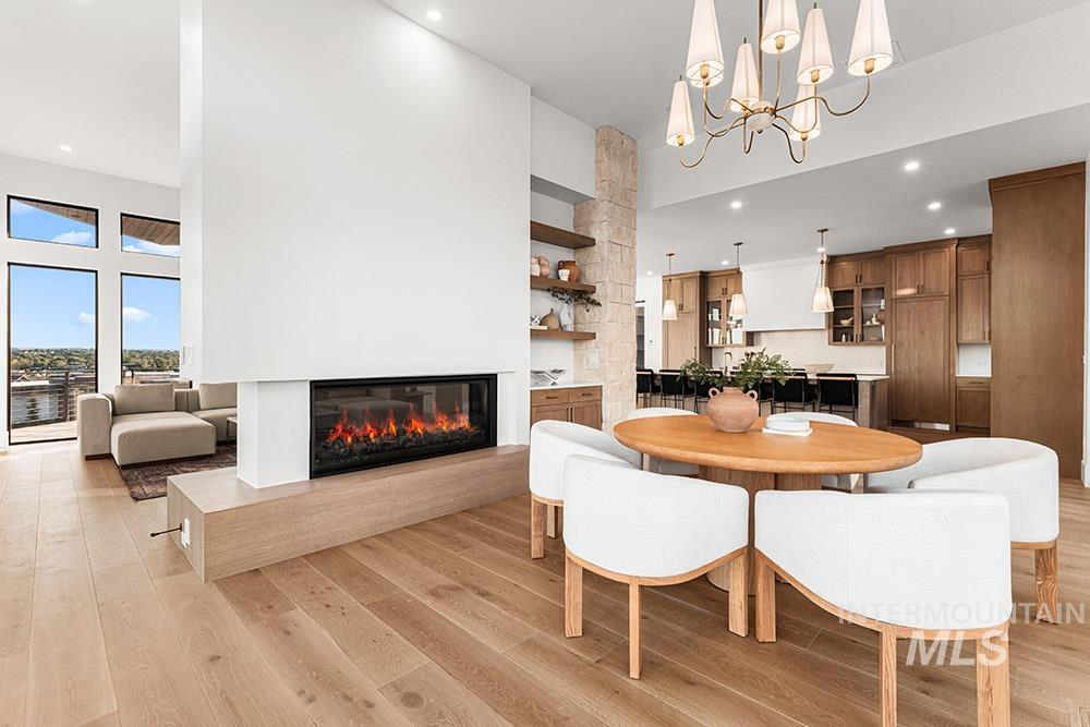 Dining room featuring light wood finished floors, a towering ceiling, a glass covered fireplace, recessed lighting, and a chandelier