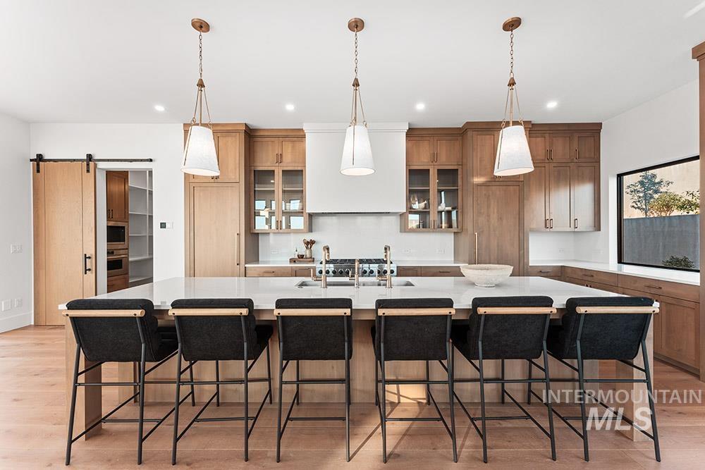 Kitchen featuring a barn door, light wood-style floors, a large island, premium range hood, and hanging light fixtures
