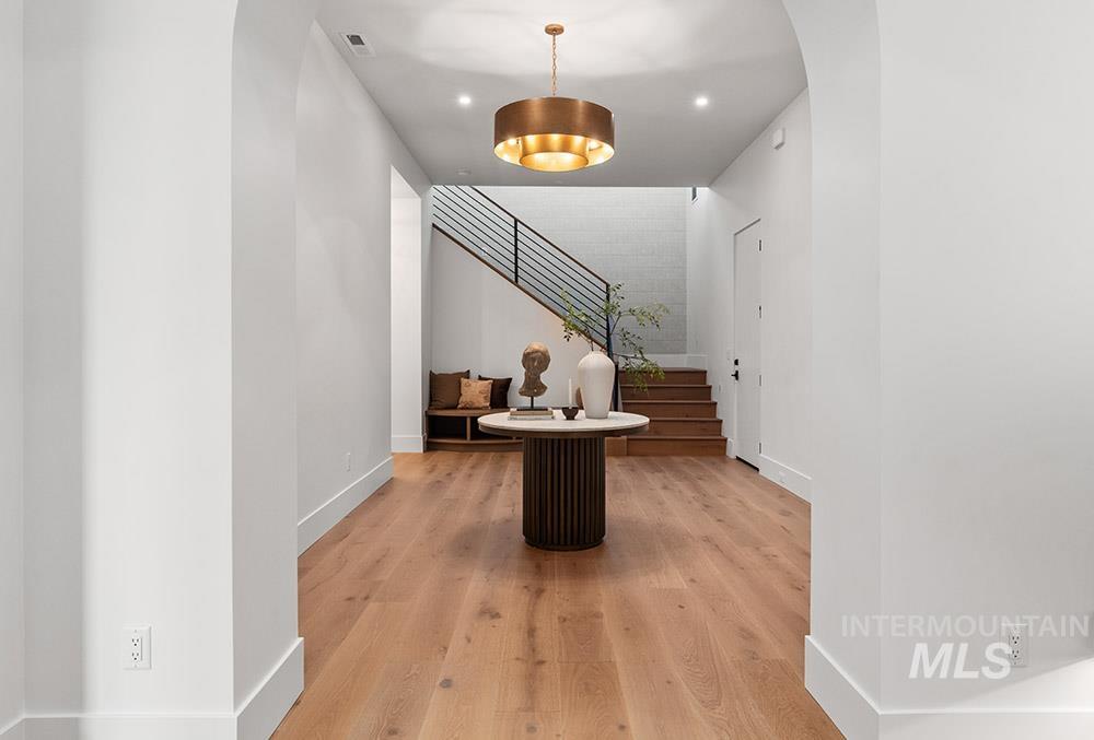 Hallway with arched walkways, light wood finished floors, stairway, and recessed lighting
