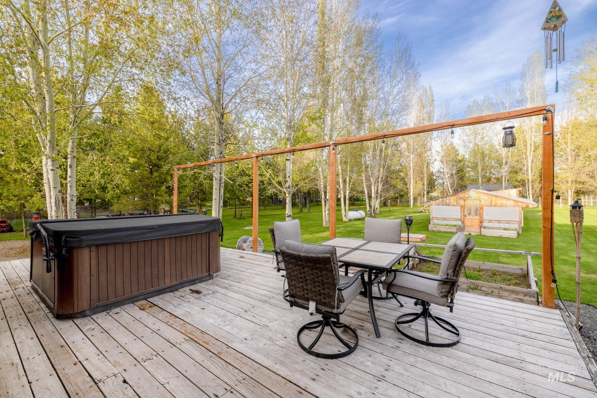 Wooden terrace with outdoor dining space, a lawn, a hot tub, and view of wooded area