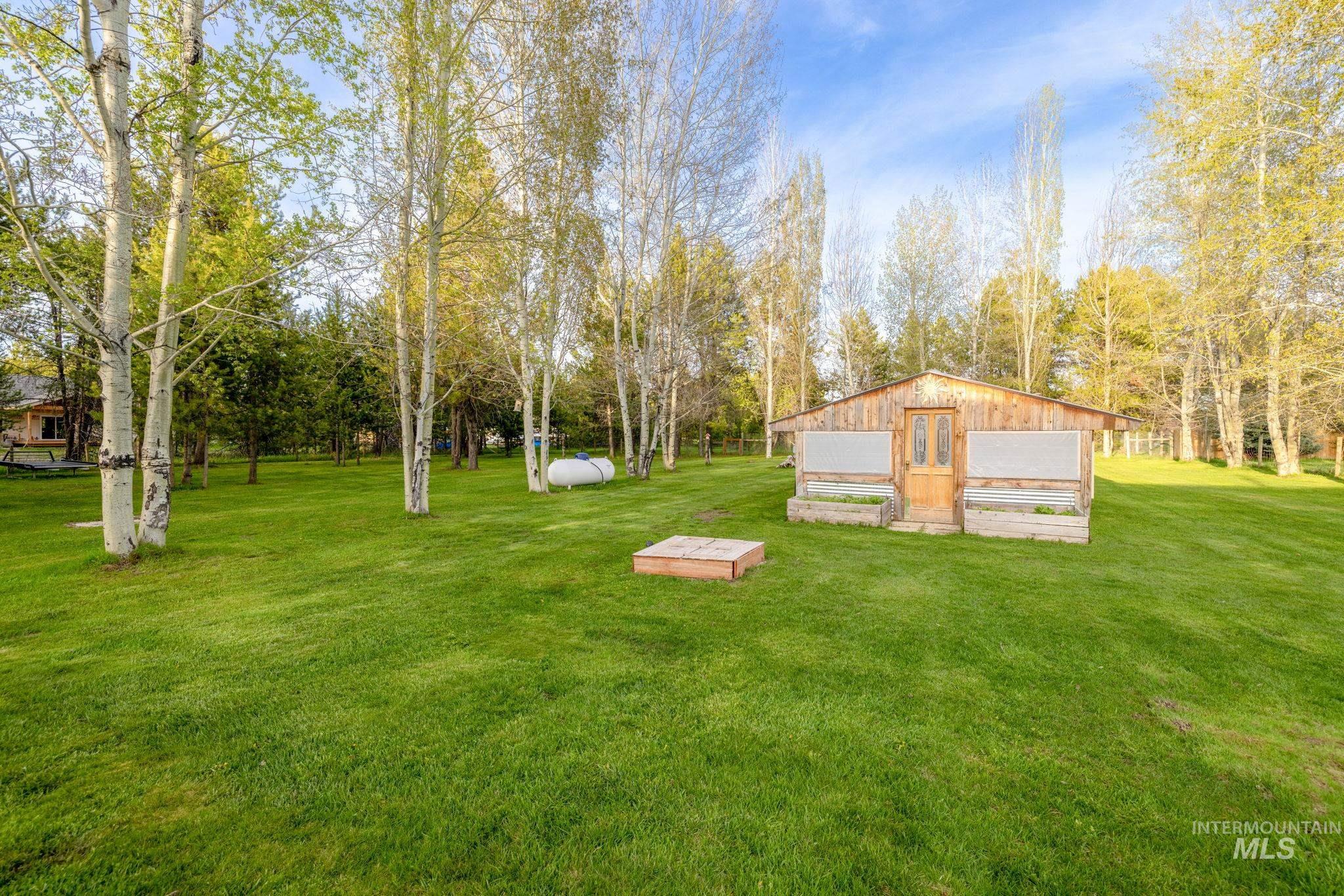 View of grassy yard featuring an outdoor structure, a detached garage, and view of wooded area