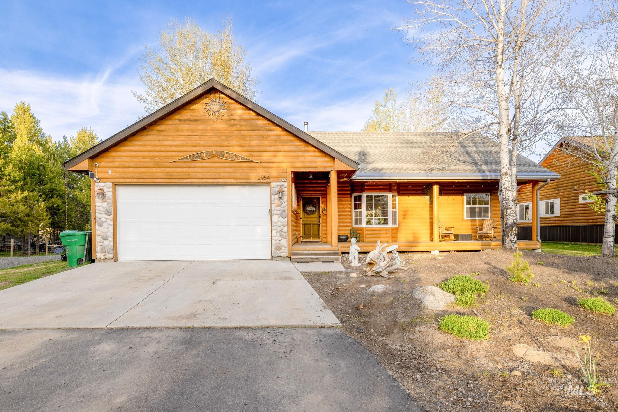 View of front of house with stone siding, a garage, driveway, covered porch, and a shingled roof