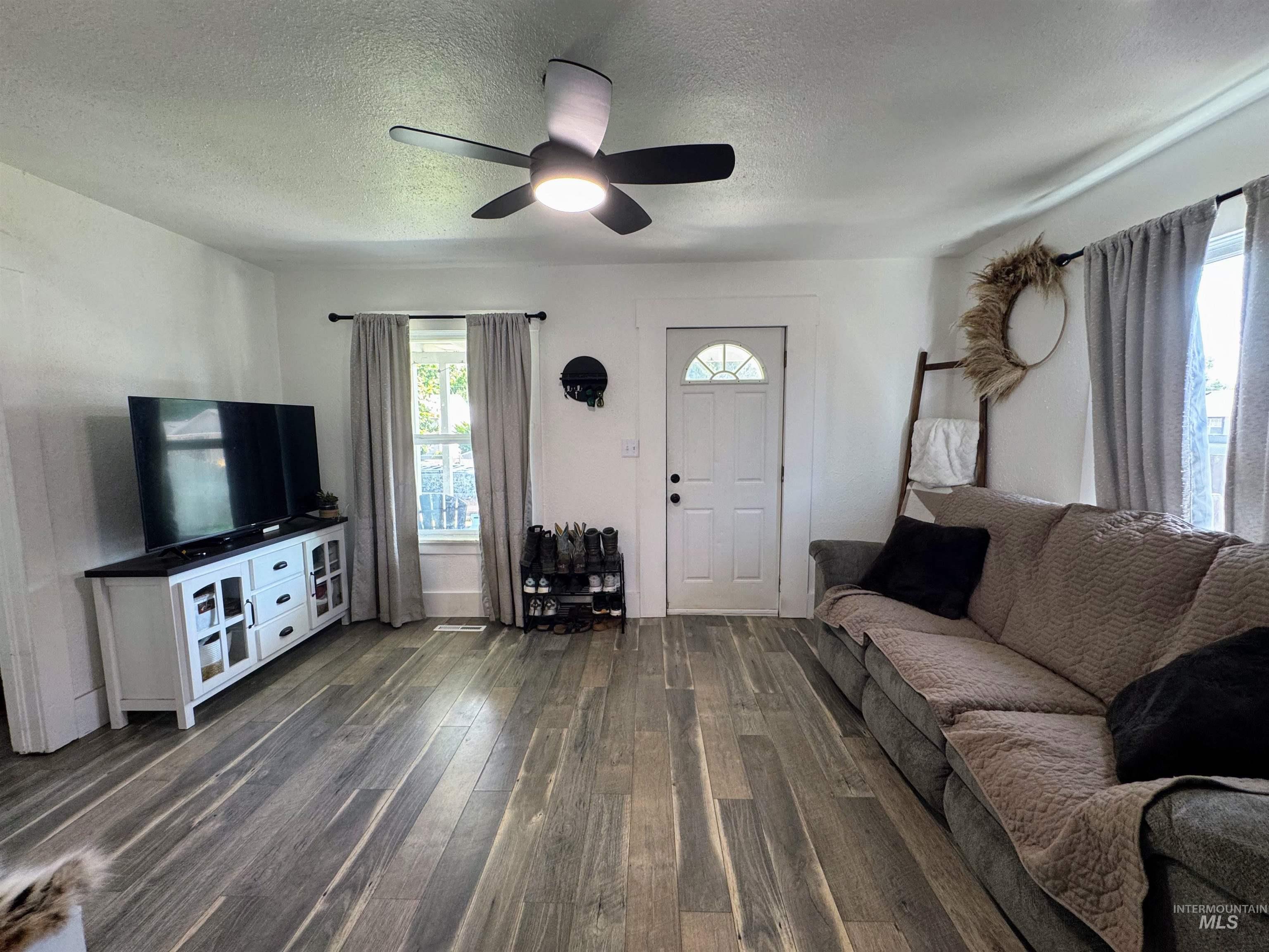 Living room with a textured ceiling, ceiling fan, and dark wood-style floors