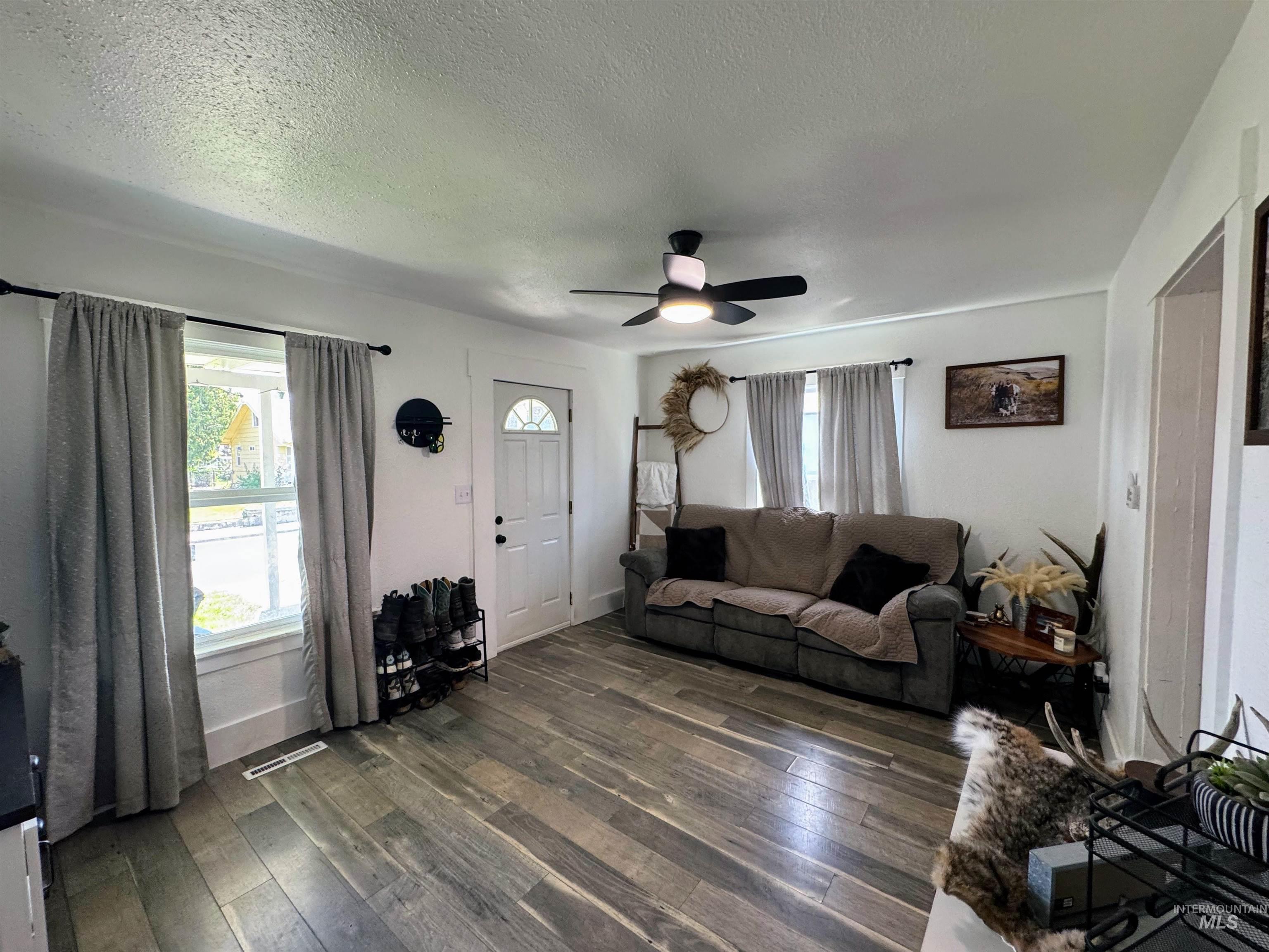 Living area with a textured ceiling, healthy amount of natural light, dark wood-style flooring, and a ceiling fan