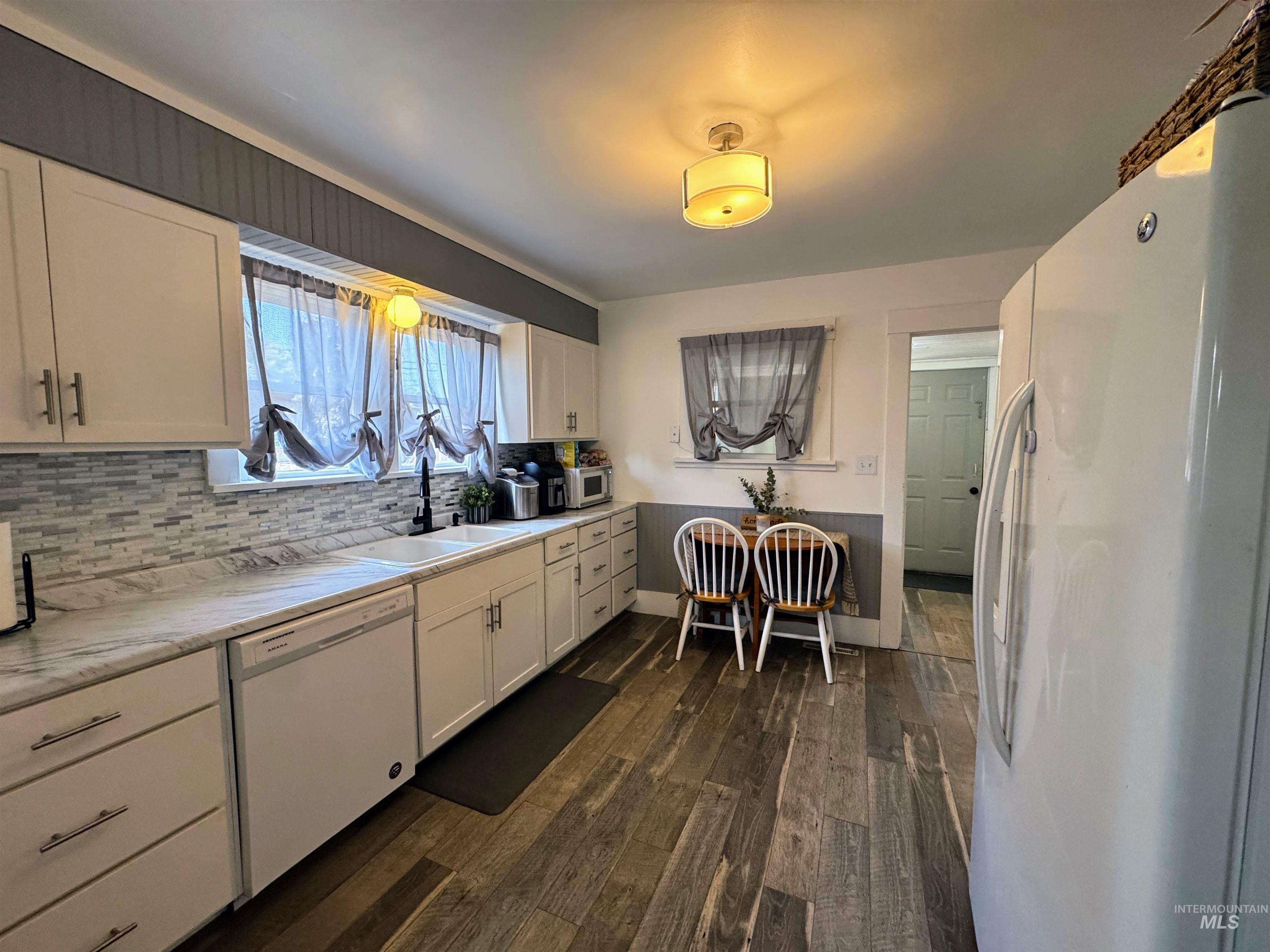 Kitchen with white appliances, white cabinets, and backsplash