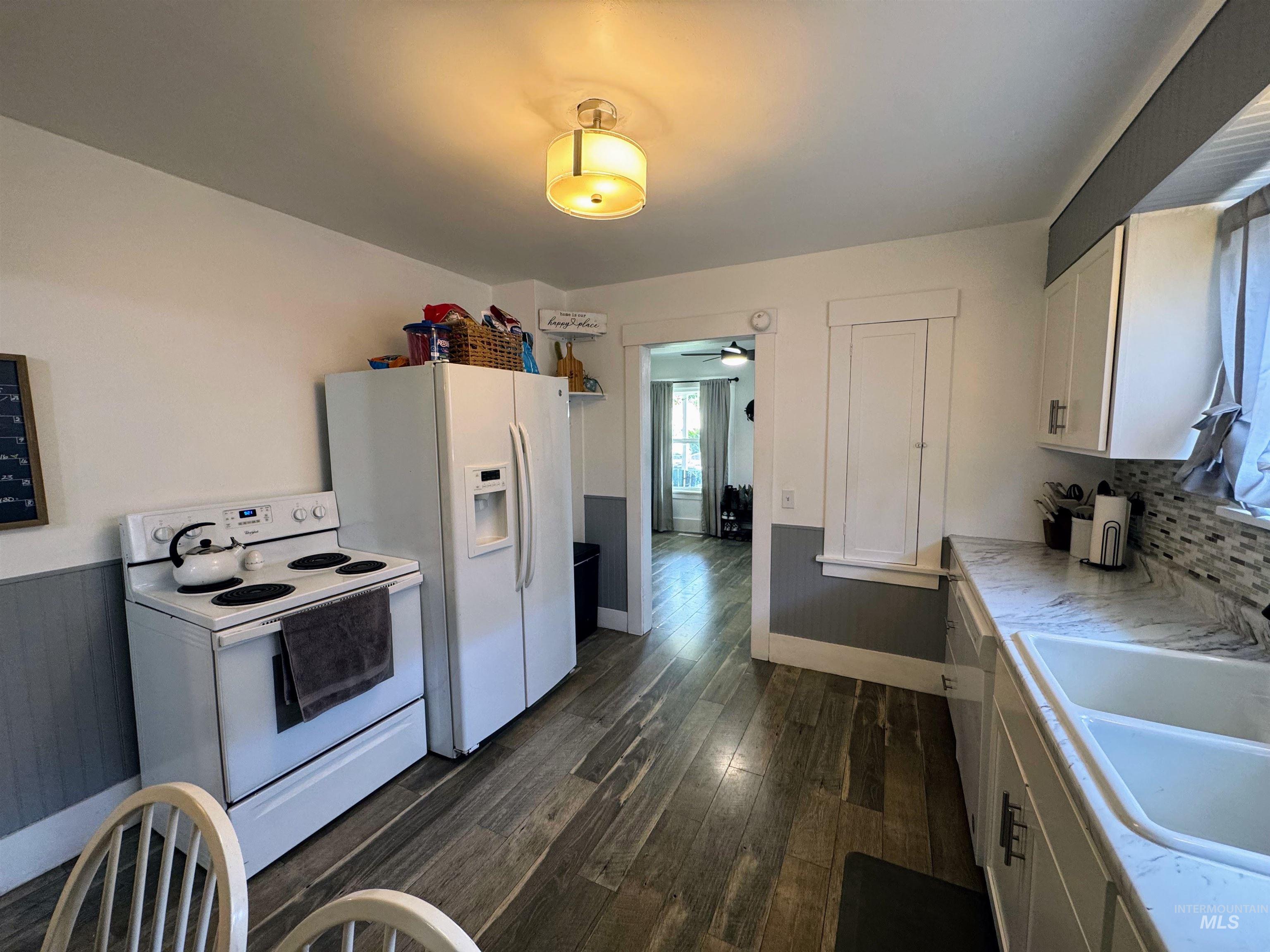 Kitchen featuring white appliances, dark wood-type flooring, light countertops, white cabinetry, and ceiling fan