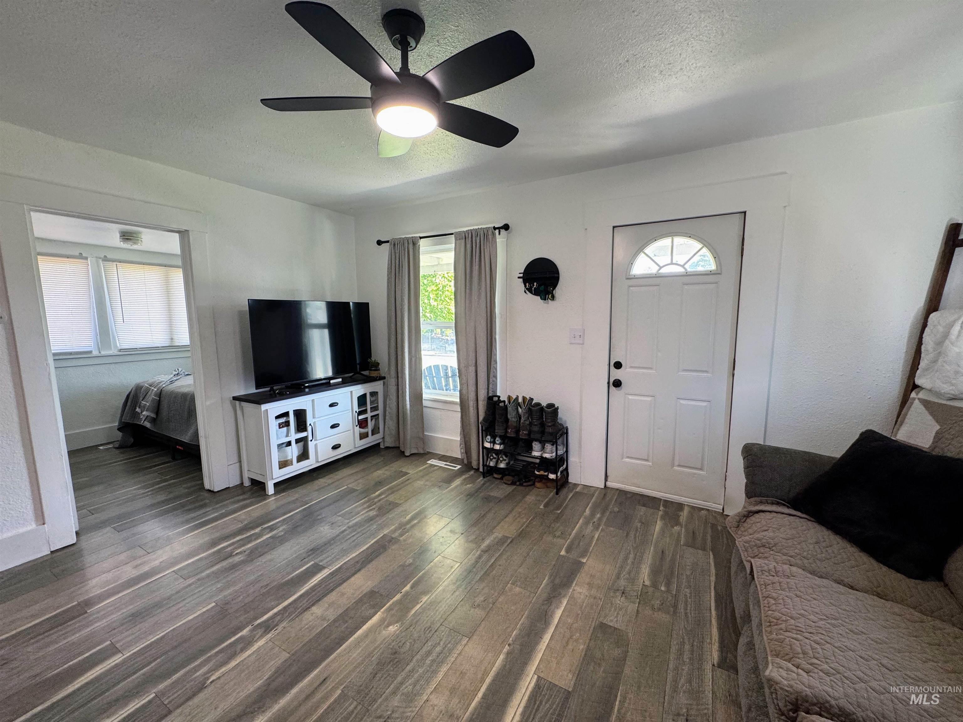Living area with a textured ceiling, dark wood-style flooring, and ceiling fan