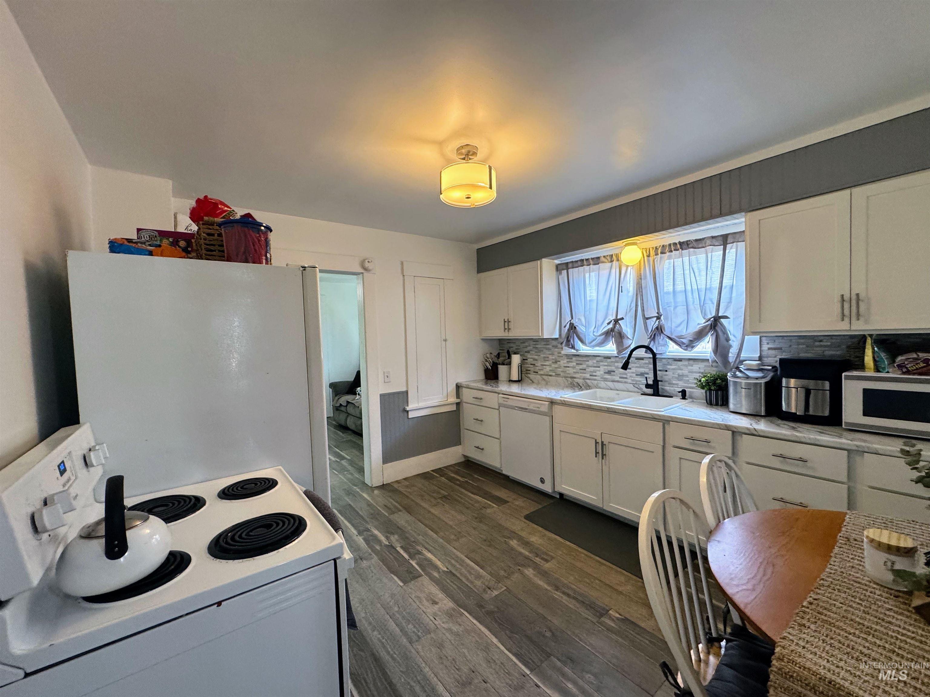 Kitchen with white appliances, light countertops, white cabinets, dark wood finished floors, and backsplash