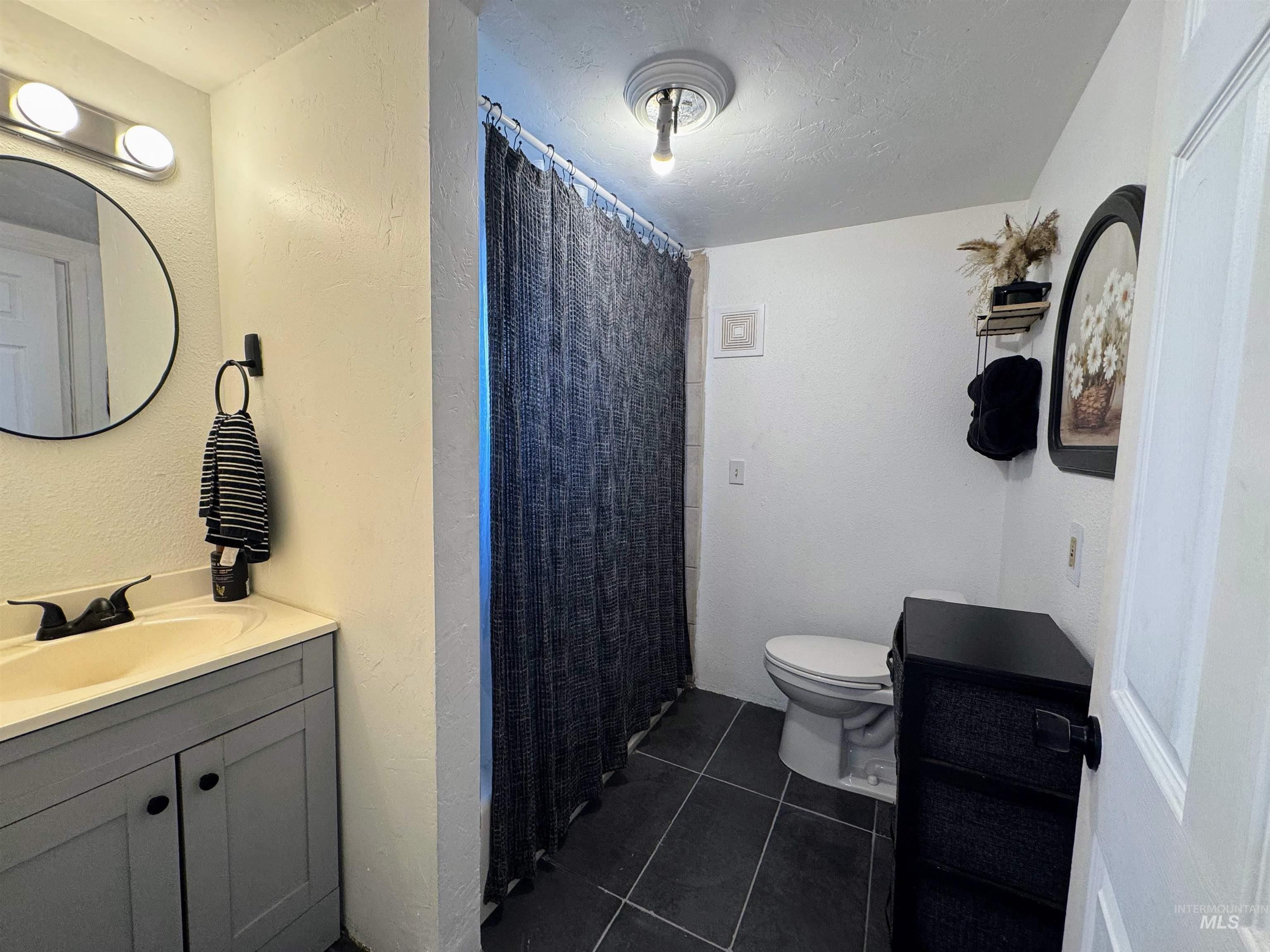 Full bathroom with vanity, tile patterned floors, a textured ceiling, a shower with curtain, and a textured wall