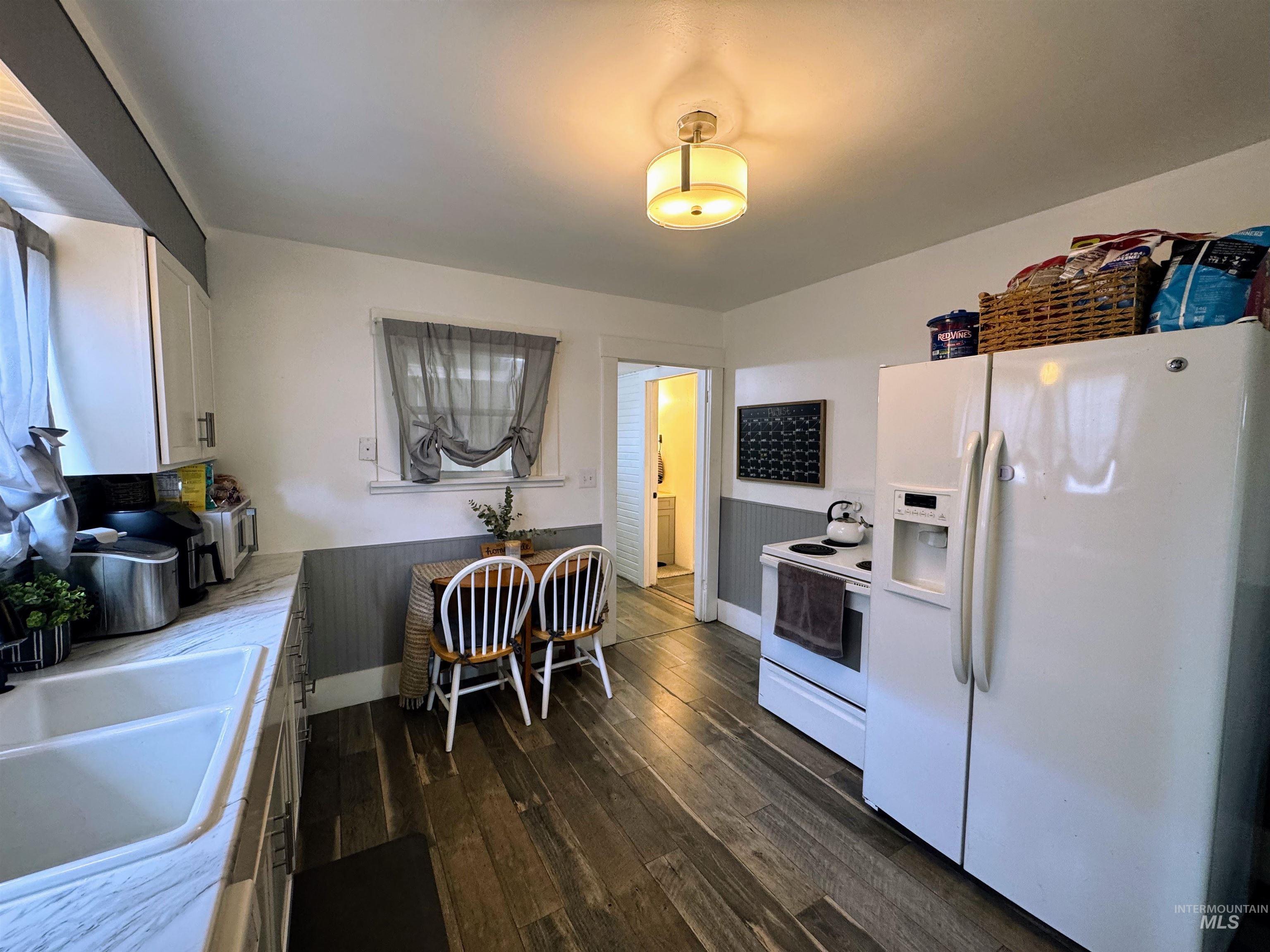Kitchen featuring white appliances, white cabinets, dark wood-style flooring, and light countertops