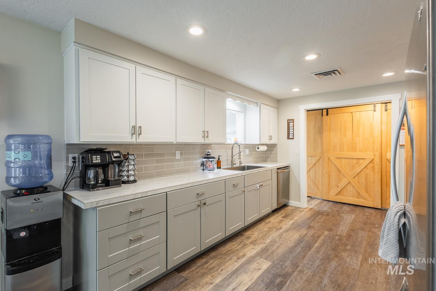 Kitchen with gray cabinets, stainless steel appliances, light wood finished floors, light countertops, and decorative backsplash