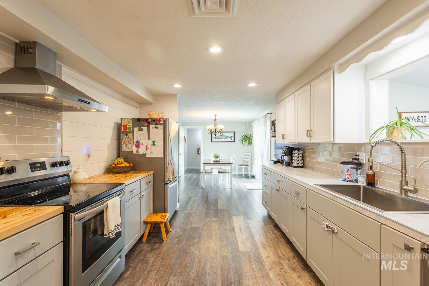 Kitchen featuring stainless steel appliances, backsplash, range hood, dark wood finished floors, and recessed lighting