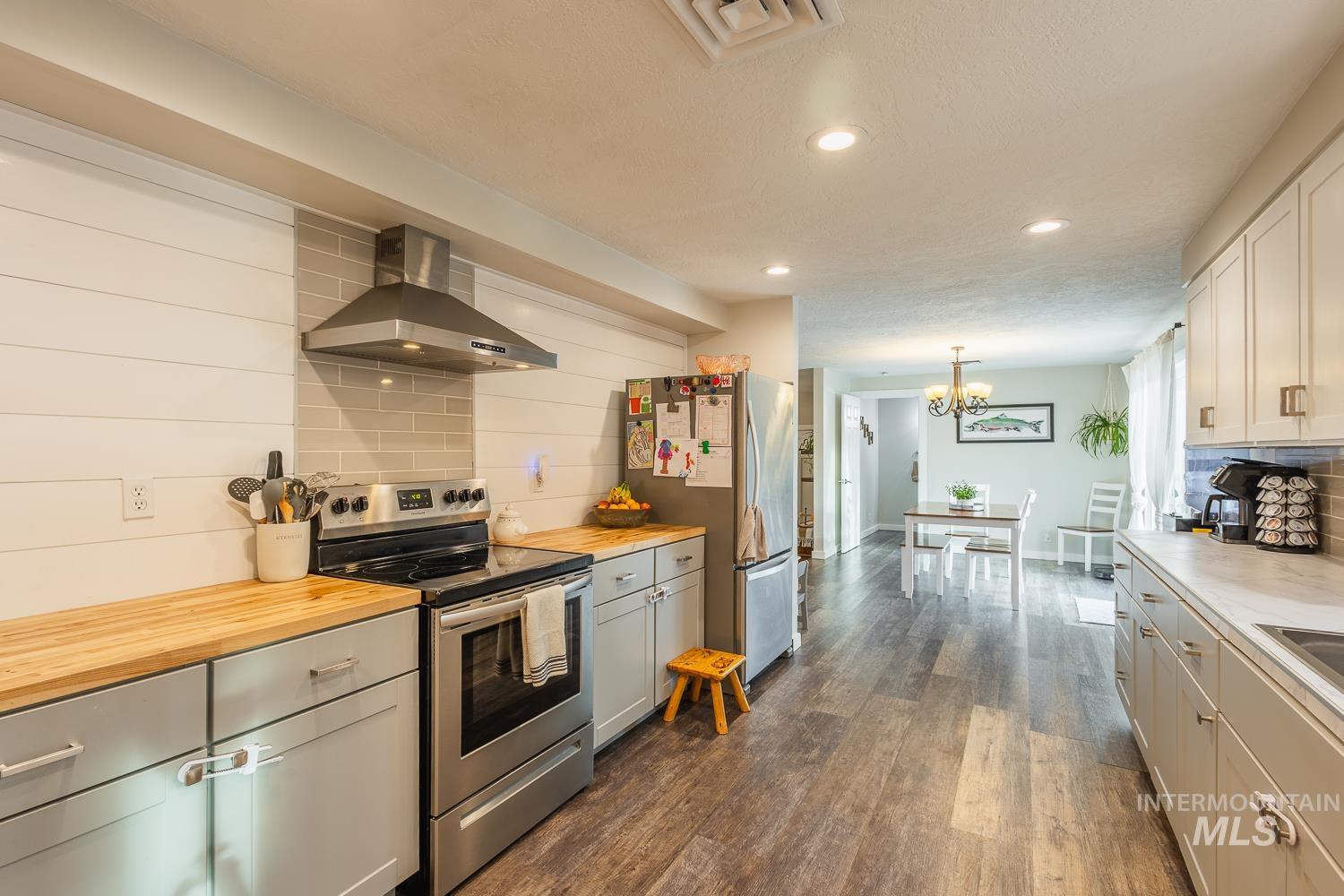 Kitchen with decorative backsplash, stainless steel appliances, extractor fan, decorative light fixtures, and dark wood-type flooring
