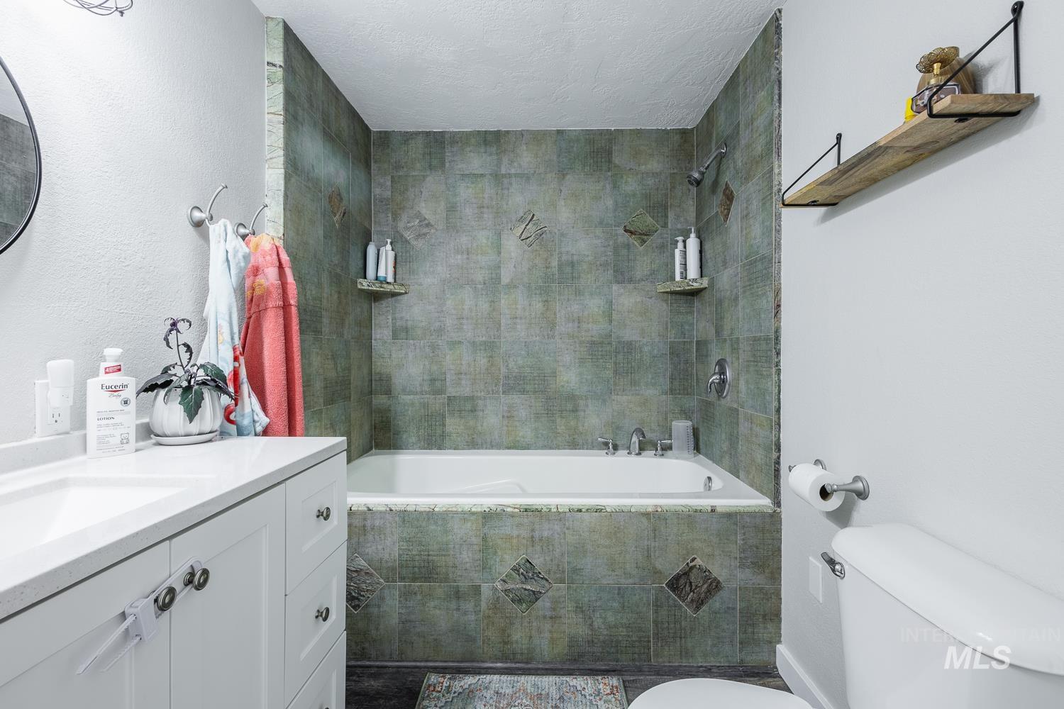 Bathroom featuring vanity, tiled shower / bath combo, a textured wall, and a textured ceiling